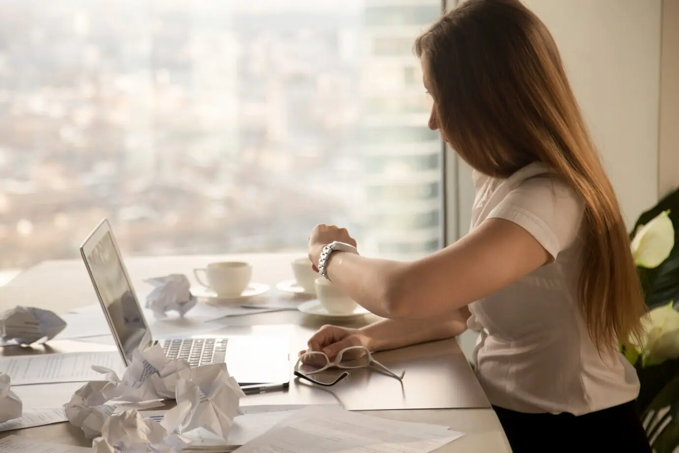 Mujer de negocios sobrecargada de trabajo mirando su reloj de pulsera, comprobando la hora para cumplir con la fecha límite.