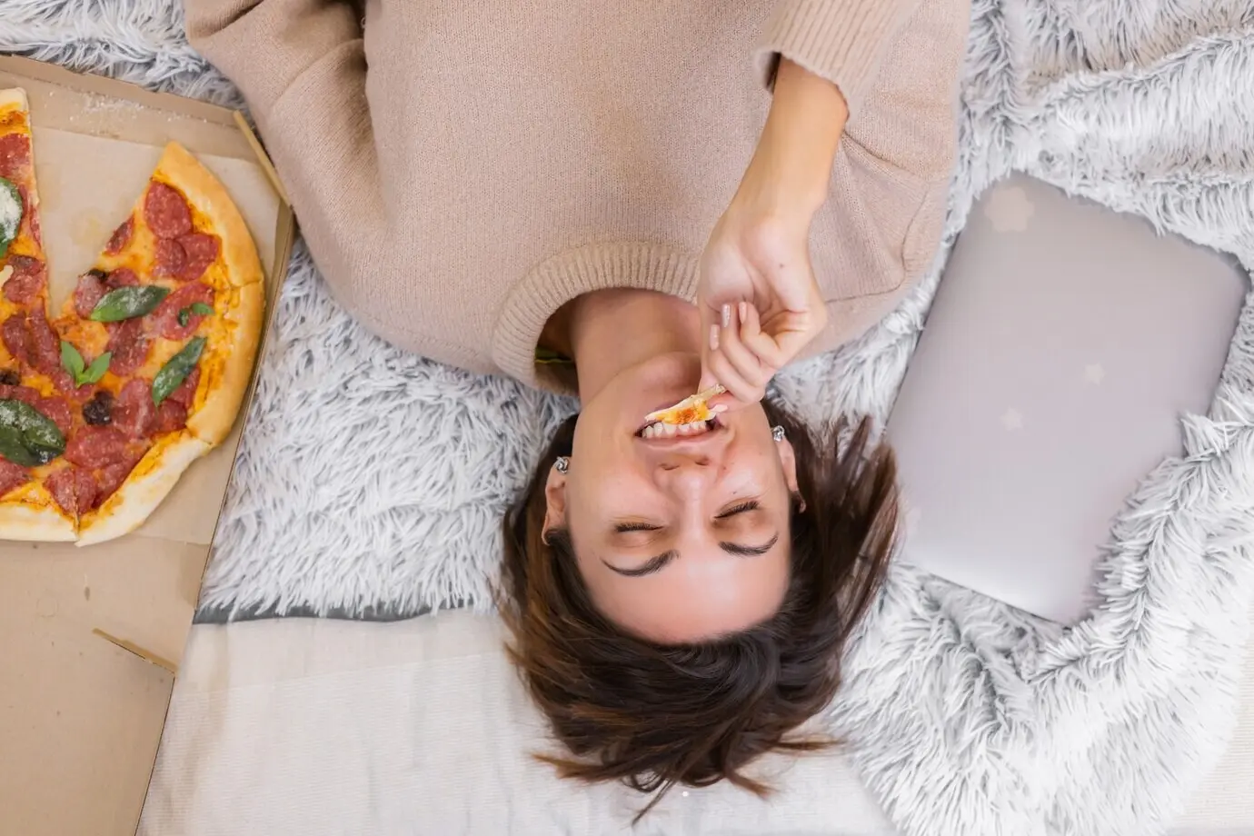 Una mujer come comida rápida a domicilio en la cama del dormitorio en casa. Sola, disfruta de comida grasosa, pizza.